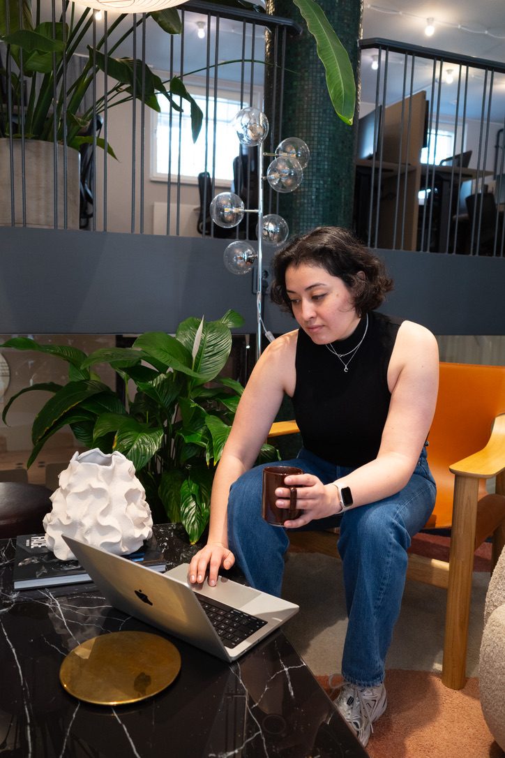 Cristina working on her laptop with a coffee, in a bright workspace