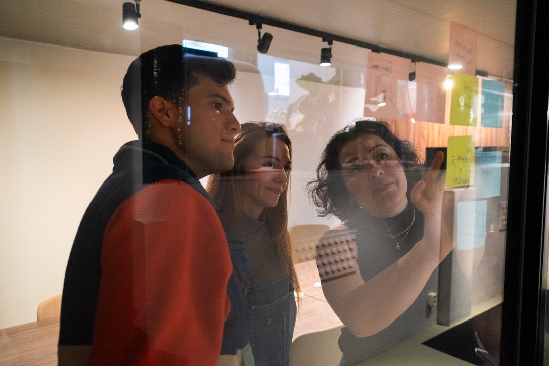 Cristina pointing at sticky notes on a glass wall while two colleagues follow along